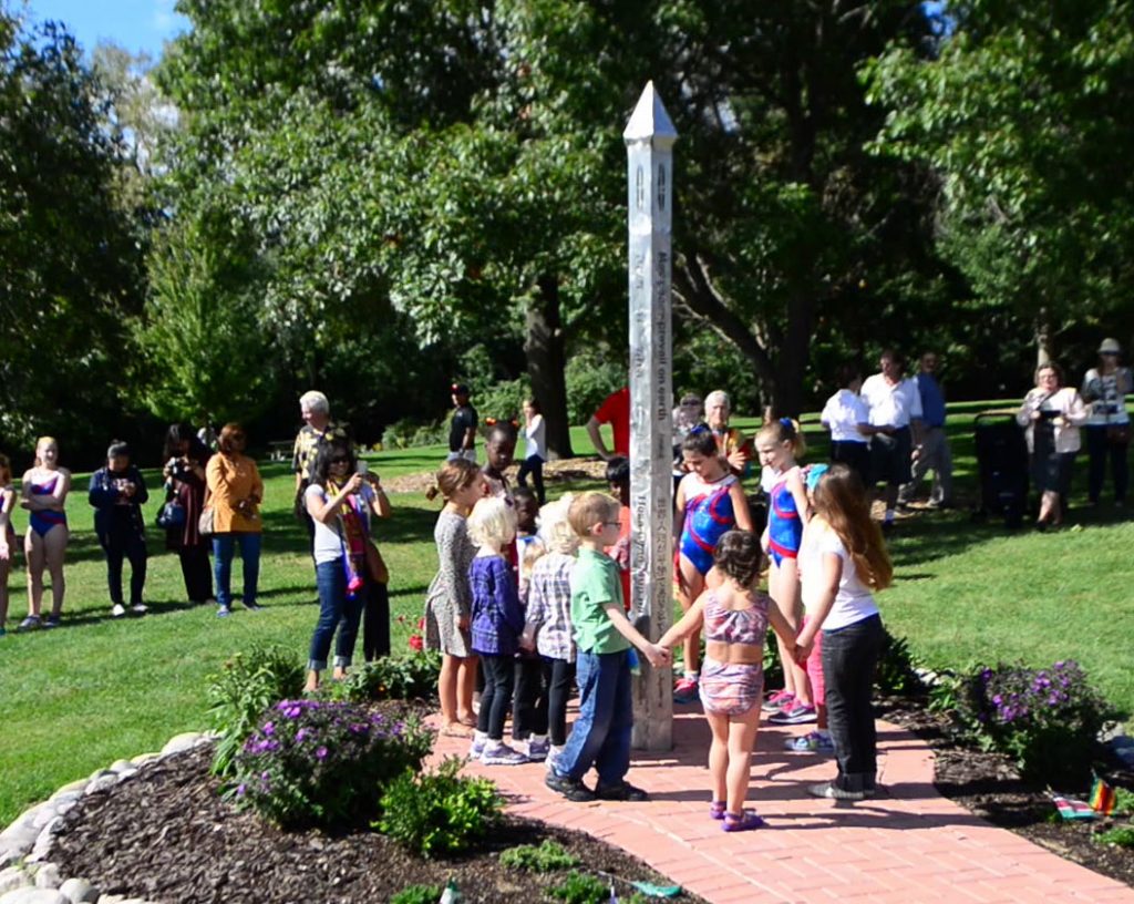 Children in procession around a stainless steel peace pole